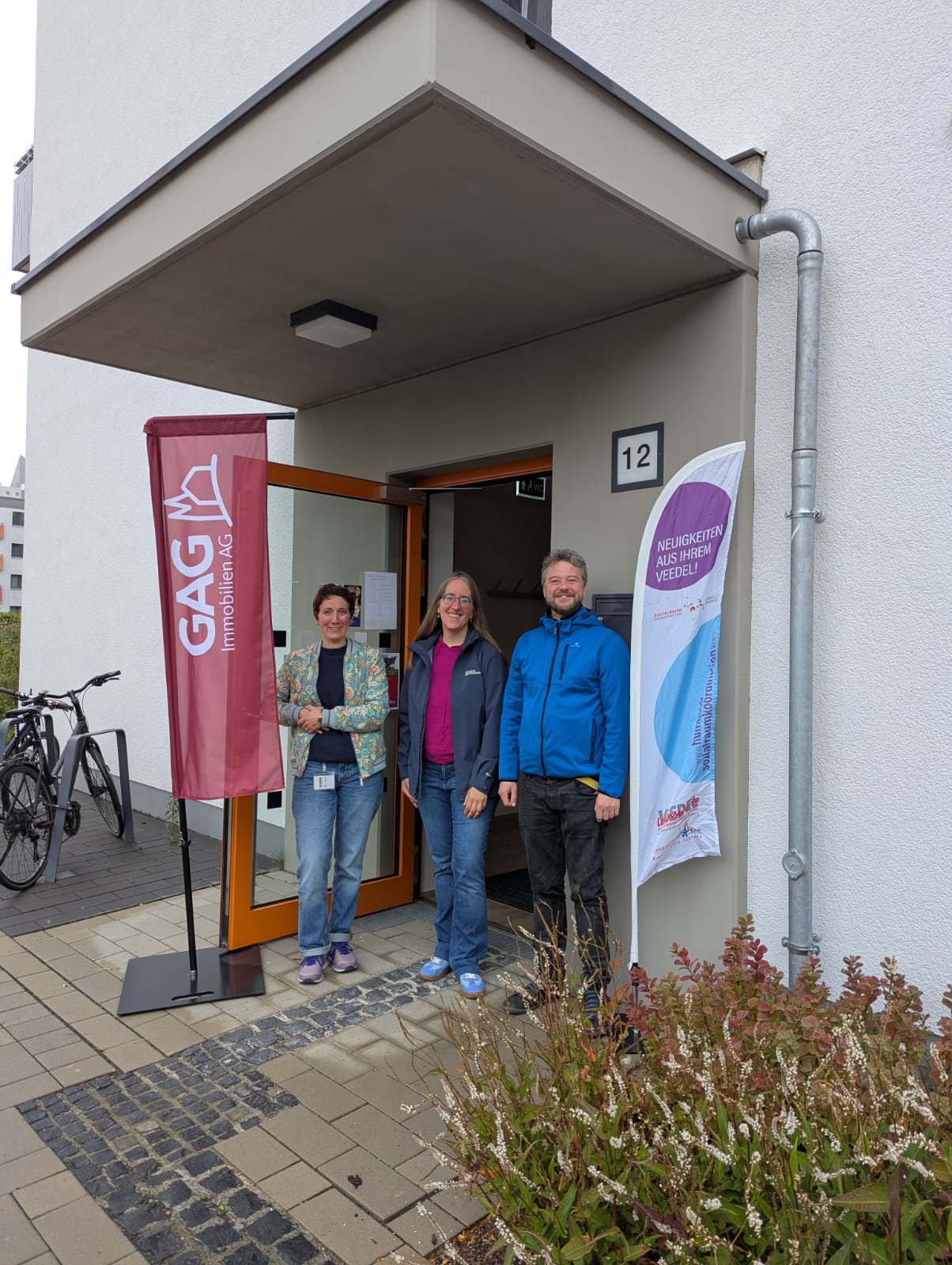 Auf dem Bild stehen drei Personen vor einem Hauseingang.